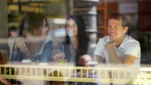 Un hombre con dos mujeres increíbles bebiendo cócteles en un café. Tres amigos son vistos a través de la ventana del restaurante . — Vídeos de Stock