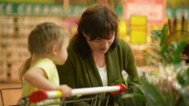 Küçük tatlı kız bir sepeti oturur ve Büyükanne bir süpermarkette alışveriş yapmak yardımcı olur.