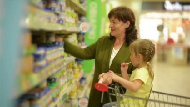 La abuela y la nieta están comprando artículos en el centro comercial. Nieta está sentada en carritos de compras . — Vídeos de Stock