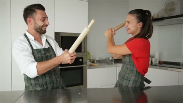 Pareja divertida fingiendo luchar con herramientas de utensilios mientras se cocina en casa juntos. Esposo y esposa divirtiéndose sintiéndose juguetón sosteniendo utensilios de cocina luchando en la cocina . — Vídeo de stock