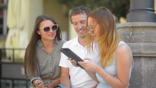 Due ragazze e un uomo con note, penne e tablet trascorrere del tempo fuori. All'aperto Ritratto di tre studenti sorridenti che parlano e si chiudono insieme all'aperto seduti sulla panchina . — Video Stock