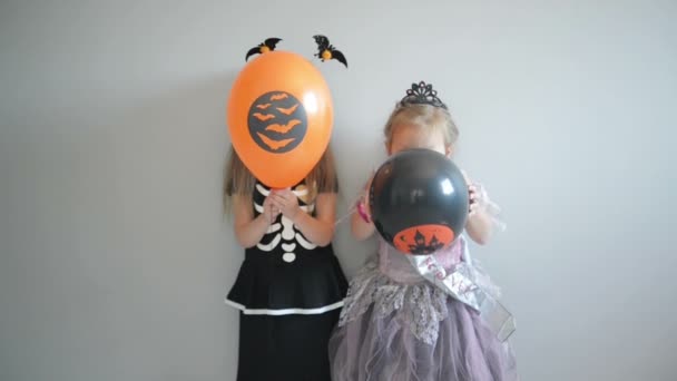 Paar van twee kleine meisjes glimlachend gekleed In kostuums van Halloween die lucht ballonnen en poseren. — Stockvideo