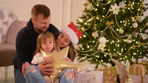 Mutter, Vater und kleine Tochter. liebe Familie frohe Weihnachten und ein glückliches neues Jahr. fröhliche hübsche Menschen. Eltern und Kind vergnügen sich in der Nähe des Weihnachtsbaums. — Stockvideo