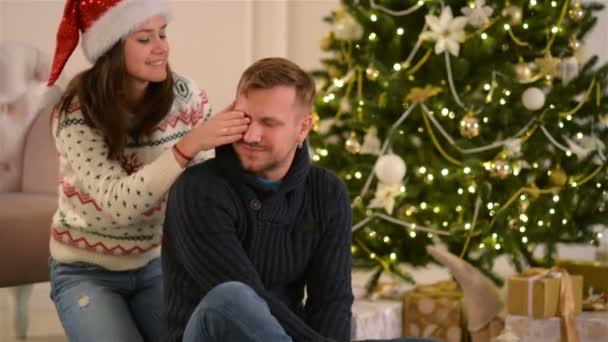 Bella giovane coppia innamorata che indossa i cappelli di Babbo Natale, sdraiata sul pavimento accanto a un camino e un albero di Natale ben decorato e godendo mattina di Natale . — Video Stock