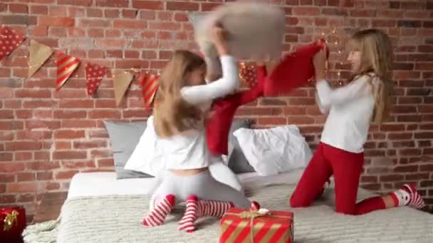 穿着睡衣的三胞胎姐妹用枕头安排了战斗。卧室装饰圣诞花环和圣诞礼物。三胞胎女孩。圣诞快乐新年快乐. — 图库视频影像