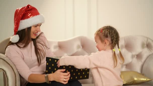 Glad mamma och hennes söta dotter baby öppna en gåva. Förälder och litet barn ha roligt nära julgran inomhus. Kärleksfull familj god jul och gott nytt år. — Stockvideo