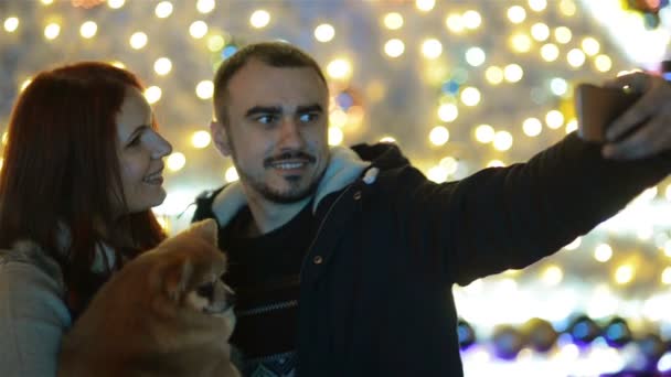 Coppia con Cutie Dog Making Selfie all'aperto davanti all'enorme albero di Natale. Buona famiglia di umore . — Video Stock