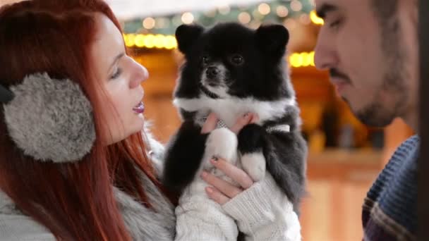 Par älskare krama med en Cutie hund. Tillsammans har de gott humör. Klädd Ward, julbelysning bakom. — Stockvideo