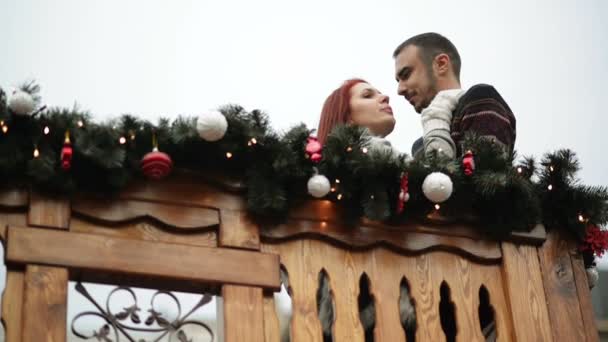Navidad. Pareja joven en el balcón de madera decorado por unas vacaciones. Cita romántica. Ayuntamiento . — Vídeo de stock