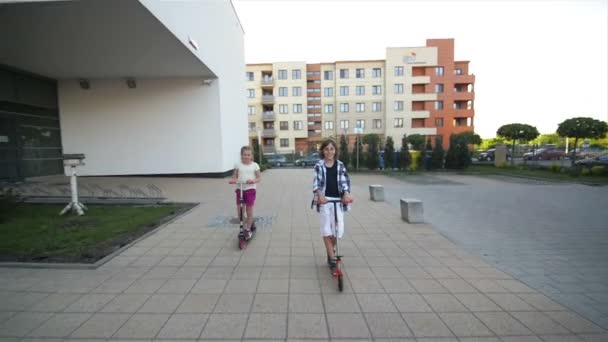 Menina e Boy Riding Kick Scooter ao ar livre. Happy Cute Children Brincando na Rua Aprendendo a Equilibrar no Kick Board no Campo . — Vídeo de Stock