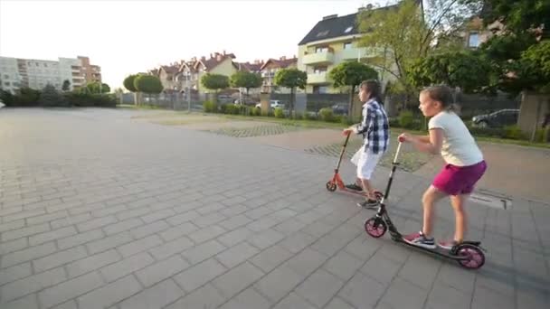 I bambini imparano a cavalcare lo scooter nella giornata estiva soleggiata. I bambini giocano all'aperto con gli scooter. Tempo libero attivo e sport all'aperto per bambini . — Video Stock