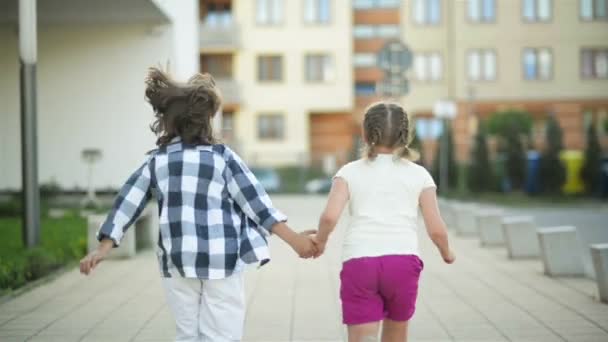 Δύο χαρούμενα παιδιά τρέχουν μαζί πιασμένοι χέρι χέρι. Τους κύμα ξανθά μαλλιά έξω στον άνεμο. — Αρχείο Βίντεο