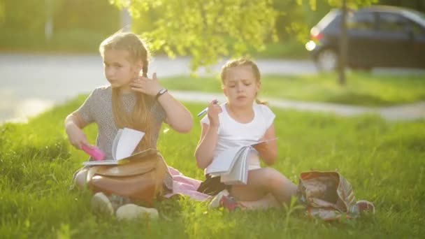 夏の庭で宿題をしている女の子。彼らは多くの知識を得る楽しみを抱えています。. — ストック動画