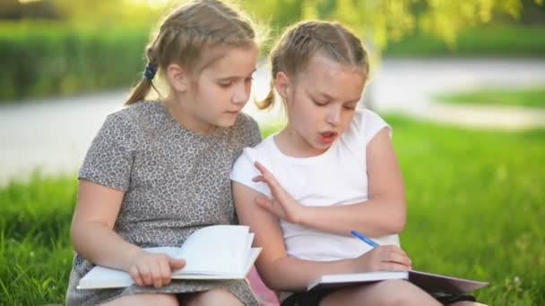Barnen läsa en bok i sommarträdgården. Förskola vänner spelar och lärande. Flickor gör sina läxor. — Stockvideo