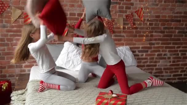 Drieling zusters in pyjama's hebben gerangschikt kussens strijd. De slaapkamer is ingericht door Kerstmis slingers en xmas geschenken. Meisjes drieling. Prettige kerstdagen en gelukkig Nieuwjaar. — Stockvideo