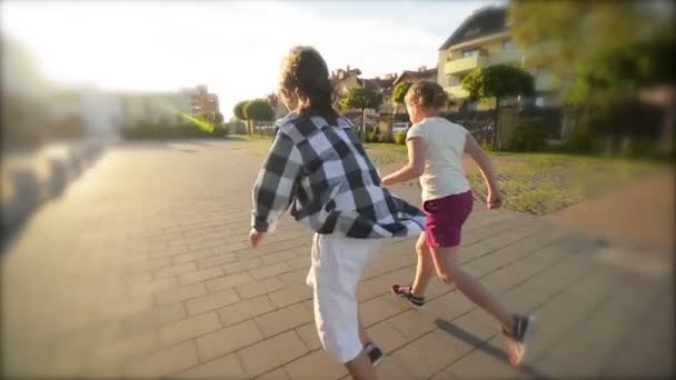Ευτυχισμένα παιδιά τρέχει μαζί πιασμένοι χέρι χέρι στο δρόμο. Οι ακτίνες του ήλιου που λάμπει στα πρόσωπά τους. — Αρχείο Βίντεο