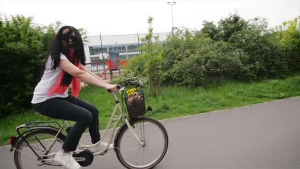 Retrato de la joven feliz en bicicleta. En su cesta de la bicicleta hay flores y una bolsa. Ella disfruta el viaje . — Vídeo de stock