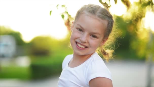 Nahaufnahme Porträt eines blonden europäischen kleinen Mädchens, das mit allen Zähnen lächelt. Ein fröhliches Kind an einem sonnigen Nachmittag sorgt dafür, dass sich alle Eltern wohlfühlen. Kindliches Lächeln ist eine Quelle positiver Emotionen. — Stockvideo