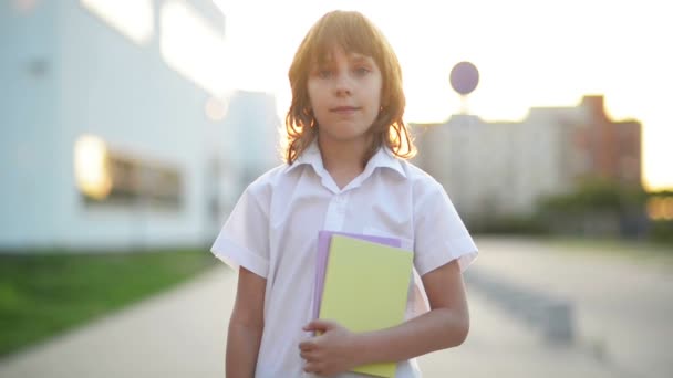 Primer plano Retrato de un chico europeo. Él sostiene un libro en sus manos. Su sonrisa es hermosa. Lleva uniforme escolar. . — Vídeos de Stock