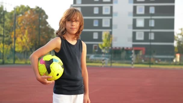スポーツ少年のポーズします 彼はサッカー ボールを保持しています 少年は良い気分です 子供の笑顔 アウトドア アクティブ — ストック動画