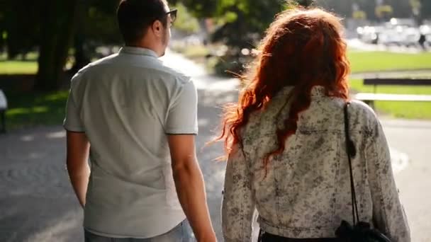 Молодая пара, держащаяся за руки, когда они идут по улицам города вместе, разговаривая и улыбаясь . — стоковое видео