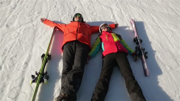 Χαρούμενο ζευγάρι των σκιέρ βάζοντας κάτω στο χιόνι. Μικρά παιδιά έχουν πολλή διασκέδαση δαπάνες χειμερινές διακοπές στα βουνά. — Αρχείο Βίντεο