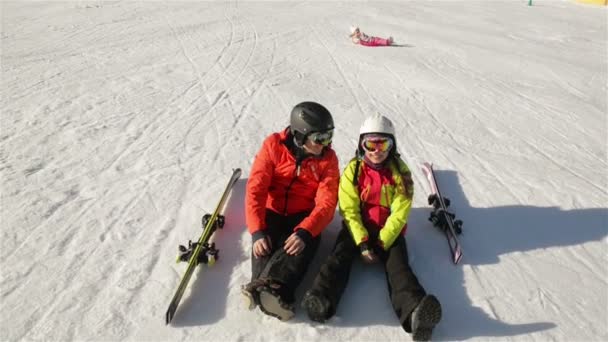 Alegre pareja de esquiadores acostados en la nieve. Los chicos jóvenes se divierten mucho pasando las vacaciones de invierno en las montañas . — Vídeos de Stock