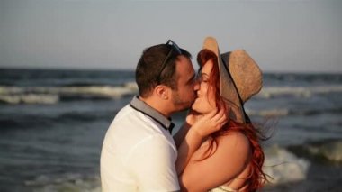 Romantik çift öpüşme ve sahilde günbatımı sırasında sarılma. Yumuşak güneşli renkler. Arka planda bkz..