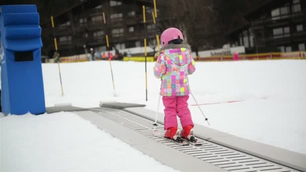 Kleines Mädchen im Winteroutfit, das auf einem Förderband steht. Kinder haben Spaß beim Skifahren. Glückliches Skivergnügen im Skigebiet. — Stockvideo