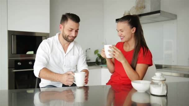 Junges Paar frühstückt in moderner Küche. weiße Kaffeetasse vorhanden. Frühstück am Morgen. glückliche Frau und Mann. romantisches Beziehungskonzept. lächelnde Menschen zu Hause. weiße Küche. — Stockvideo