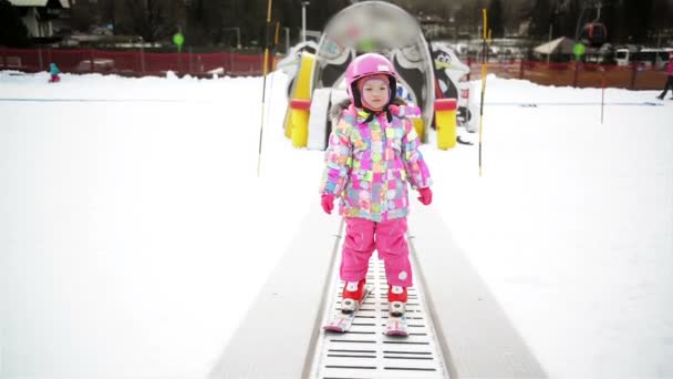 Menina em roupa de inverno ficando no transportador de esqui. O miúdo está a divertir-se, começa a esquiar. Experiência de esqui feliz no resort . — Vídeo de Stock
