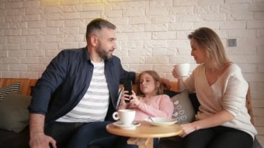Aile Cafe dinleniyor. Anne, baba ve kızı ailedir. İnsanlar masada oturuyor. Onlar mutlu ve gülümseyerek. Aile portresi. Güneşli gün.