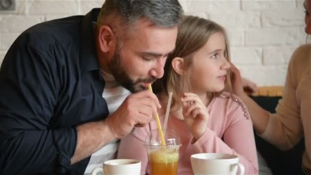 Chica joven de la adolescencia junto con su padre divertirse en el café. Están bebiendo jugo carmesí con hielo a través de un tubo y riendo . — Vídeos de Stock