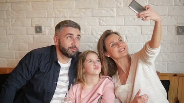 Feliz madre, padre y niña divirtiéndose y tomando selfie por teléfono inteligente en el café . — Vídeos de Stock