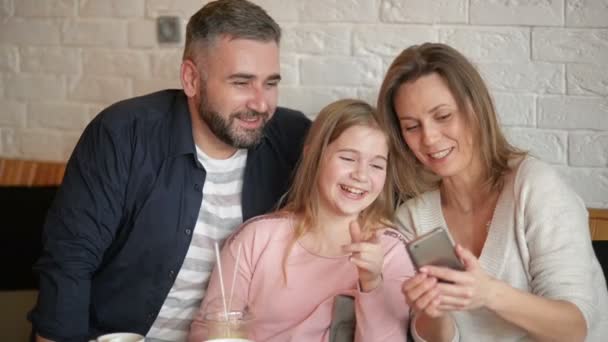 Feliz madre, padre y niña divirtiéndose y tomando selfie por teléfono inteligente en el café . — Vídeos de Stock