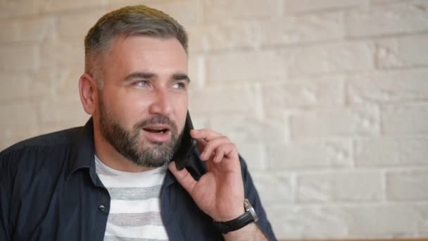 Stilig affärsman prata i telefon på Cafe. Ung skäggiga killen håller sin Smartphone nära sitt öra. Attraktiva kaukasiska mannen i vit skjorta ringer någon på hans mobiltelefon. — Stockvideo