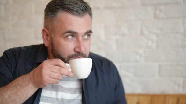 Feliz hombre de negocios caucásico en ropa formal sonriendo y mirando la pantalla de su teléfono inteligente mientras bebe café en el café interior durante la hora del almuerzo . — Vídeo de stock