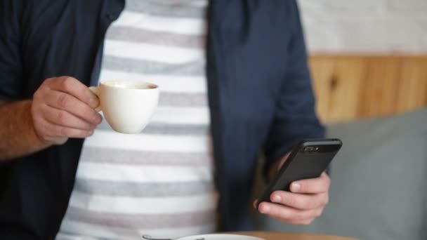 Nahaufnahme des Geschäftsmannes. Er arbeitet während des Frühstücks. Smartphone in der Hand und Kaffee oder Tee trinken. — Stockvideo