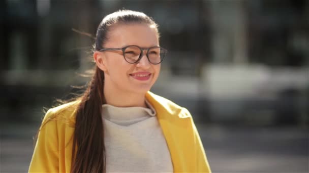 Портрет веселу усміхненим молодим діловим жінкам у жовтому пальто. Вона має дуже гарний настрій проводити час в місті. — стокове відео
