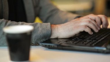 Internet Cafe kapalı dizüstü siting üzerinde Freelancer çalışma yakın görünüm. Genç sakallı adam dizüstü üzerinde düğmeler basarak metin yazıyor. Online Iş, Freelance, ofis.