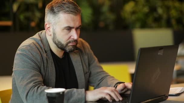 若いひげのヒップスターの男、起業家は、コーヒーテーブルでソファの上に座って、空白の画面でノートパソコンを使用しています。テーブルノートとコーヒーカップに。オンラインマーケティング、教育、E ラーニング、スタートアップ. — ストック動画
