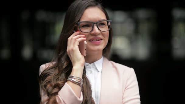 Felice giovane avvocato sta parlando al telefono in piedi su sfondo costruzione della città. Bruna abbronzata in giacca bianca sta discutendo di affari con sorriso allegro all'aperto. Concetto: persona d'affari, professionista — Video Stock