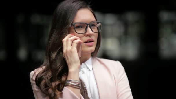 Молода кавказька Ділова жінка розмовляю по телефону і дивиться на годинник по міській будівлі міського фону — стокове відео