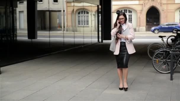 Eine junge, gestresste Geschäftsfrau mit Brille geht mit Dokumenten und Telefongesprächen durch die Stadt. Kaffeezeit. — Stockvideo