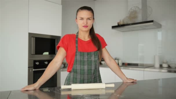 Jovem e sorridente dona de casa caucasiana no avental listrado. Camiseta vermelha isolada no fundo da cozinha. Belo retrato da empregada doméstica mulher . — Vídeo de Stock