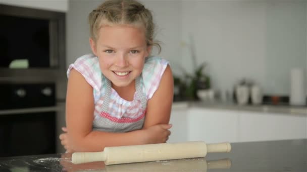 Μικρό χαριτωμένο κορίτσι μαγειρεύει στην κουζίνα. Διασκεδάζοντας ενώ κάνει κέικ και μπισκότα. Χαμογελώντας και κοιτάζοντας την κάμερα. — Αρχείο Βίντεο