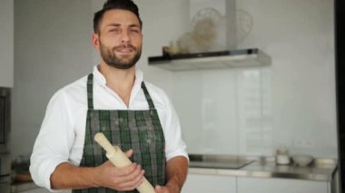 Portre, genç yakışıklı beyaz Executive Chef önlük. O Modern Lighty geniş mutfak içinde kalıyor.