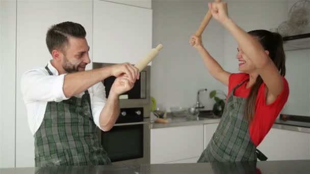 Lustiges Paar, das vorgibt, beim gemeinsamen Kochen mit Utensilien zu kämpfen. Mann und Frau haben Spaß beim spielerischen Halten von Geschirr in der Küche. — Stockvideo