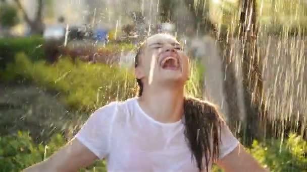 Jeune femme souriante se tient sous la pluie fraîche en été. Elle s'amuse beaucoup à passer ses vacances dans la nature . — Video