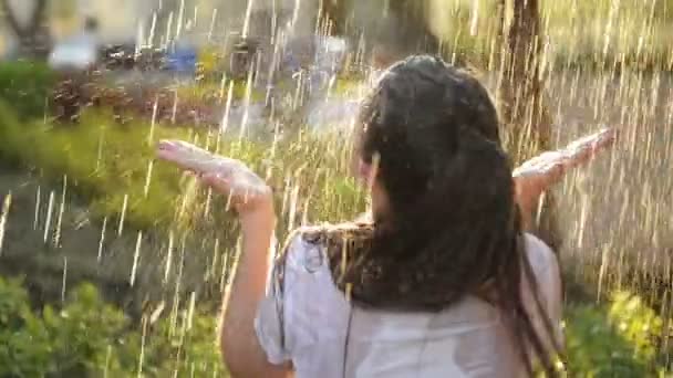 Молодая улыбающаяся женщина стоит под свежим дождем летом. Она очень весело проводит свой отпуск на природе . — стоковое видео